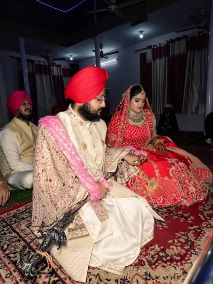 The bride and groom seated respectfully during their Anand Karaj. The groom holds the kirpan, a symbol of his duty to protect, showcasing a key element of the traditional Sikh groom's attire.