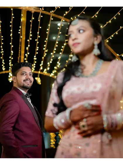 A creative shot with the groom in focus while the bride is softly blurred in the foreground, set against fairy lights.