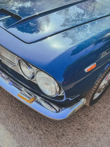A close-up on the chrome and deep blue paint of a classic car, reflecting the bright Mumbai sun.