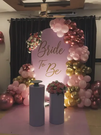 A beautiful 'Bride to Be' decoration for a bachelorette party or bridal shower. This setup uses a soft pink backdrop with elegant gold lettering, framed by an arch of pink, gold, and rose gold balloons for a celebratory feel.