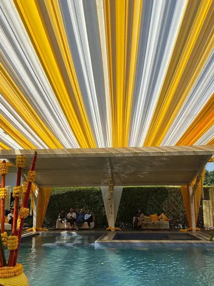 A poolside Haldi event with a vibrant canopy of yellow and white drapes. This setup provides shade while adding a festive and colorful element that perfectly complements the celebratory mood.