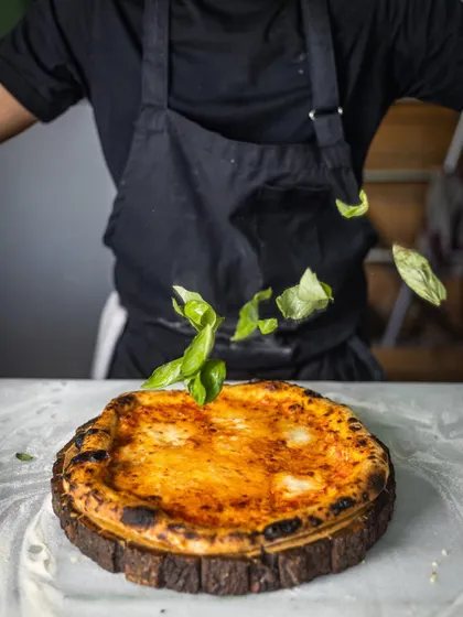 Another angle of basil leaves falling onto a hot pizza. This simple garnish adds an incredible amount of fresh, aromatic flavor.