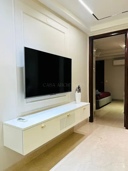 A minimalist media unit floats against a wall with classic paneling, creating a clean and sophisticated look. The open doorway offers a glimpse into a serene bedroom.