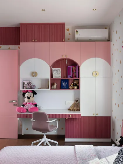A child's room should be both magical and practical. For this space, I designed a custom wardrobe and study unit in shades of pink, featuring playful arch details and integrated shelving. It's a design that provides ample storage and a dedicated homework space that can grow with them.