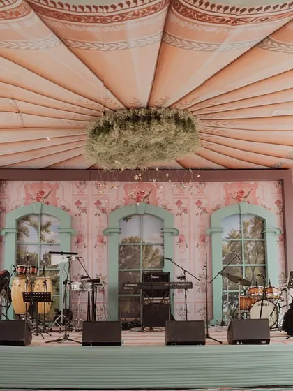 The stage for the 'Mint to Be' event, set for a musical performance. The backdrop features painted windows looking out onto a garden, and the ceiling is a custom-printed canopy with a central floral chandelier.