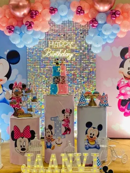 I create detailed, themed decorations for kids' birthday parties. This first birthday setup is based on a Mickey and Minnie Mouse theme, with custom character cutouts, a themed cake display, and a colorful balloon arch.