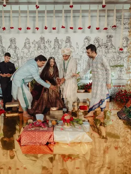 A moment during the wedding ceremony, with the family gathered inside the brass mandap. The golden, reflective floor beautifully mirrors the couple and the intricate decor, adding a layer of surreal beauty to the scene.