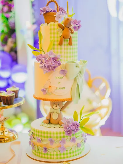 I believe the dessert table should be as beautiful as the main decor. Here, I've styled a stunning multi-tiered 'Baby in Bloom' cake, ensuring it perfectly matches the green gingham and lavender floral theme of the celebration.
