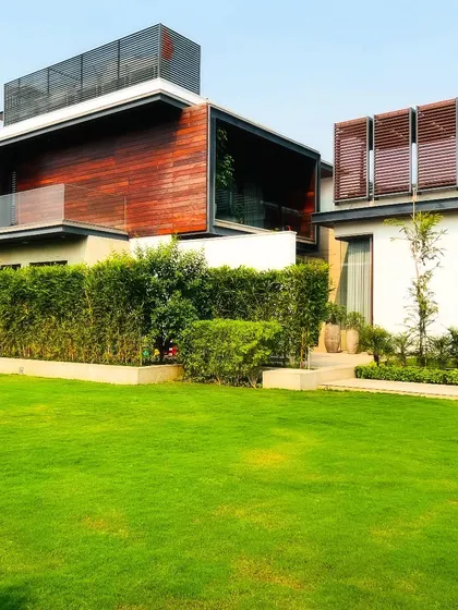 The modern architecture of this Sultanpur farmhouse is softened by the surrounding landscape. I used a combination of manicured lawns and dense, tall hedges to create a natural privacy barrier that complements the building's clean lines.