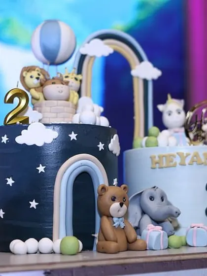 Another view of the twin animal-themed cakes, showing the detailed fondant work on the teddy bear, elephant, and hot air balloon.