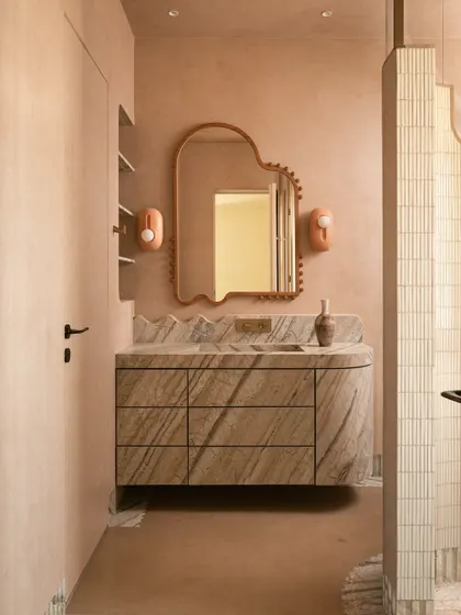 A closer look at the master bathroom, showing the organic-shaped mirror, playful sconces, and the way the marble's veining continues from the vanity down to the fluted skirting on the floor.