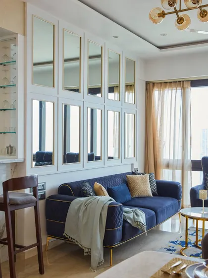 A view of the living space with a rich blue sofa and gold-accented coffee tables. The mirror paneling behind the sofa visually expands the room, reflecting light and adding a layer of sophistication.