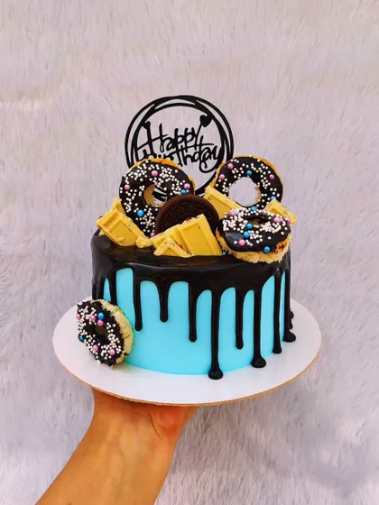 A fun drip cake topped with mini donuts, white chocolate bars, and Oreos. The bright blue buttercream provides a great pop of color.