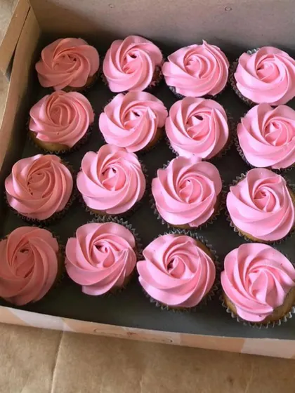 A box of delicate pink frosted cupcakes, also part of a "he or she" themed baby shower order.