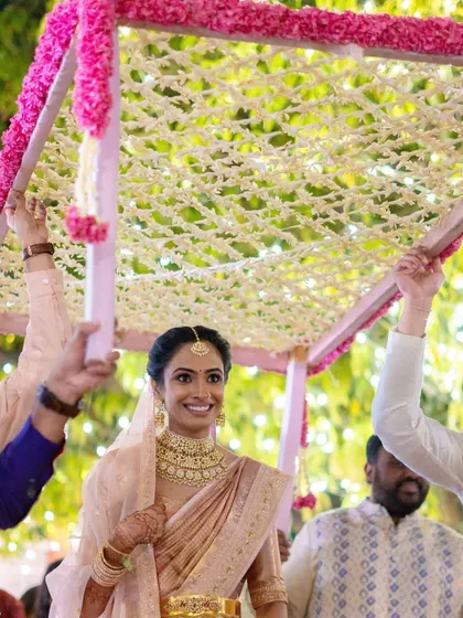 A smiling South Indian bride makes her entrance under a delicate 'phoolon ki chadar' made of jasmine.
