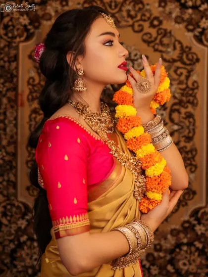 A close-up profile of a model in a traditional South Indian look. The way she holds the marigold garland near her face creates a poetic and graceful bridal portrait.