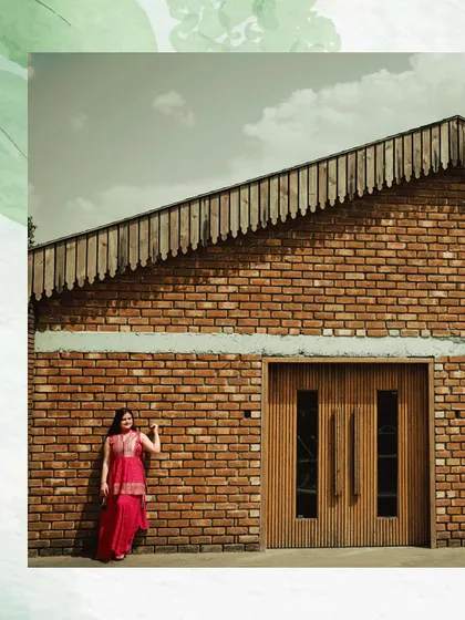 A wide-angle shot of a woman posing against a modern brick and wood building. This architectural portrait has a strong, contemporary feel.