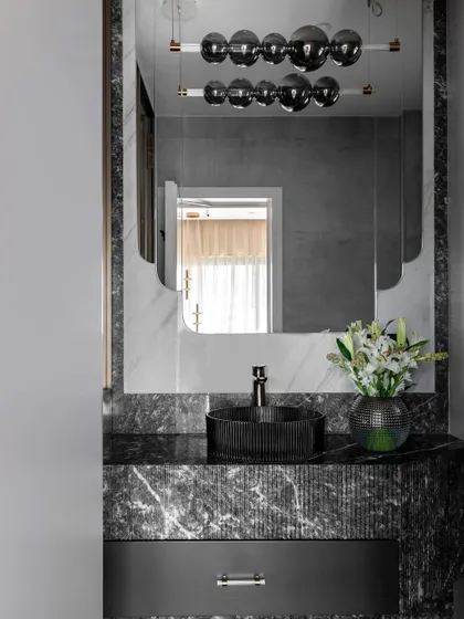 A powder room from the Evelyn project, featuring a dramatic fluted vanity made of black marble. The sleek, modern fixtures and unique bubble chandelier create a space that is both serene and luxurious.