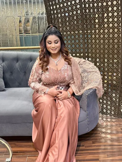 A soft and pretty party makeup look. The client is glowing with peachy tones on her cheeks and lips, complementing her rose-gold outfit.