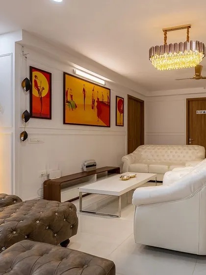 A classic and elegant living room with white Chesterfield sofas and tufted leather ottomans. The space is personalized with colorful paintings and a beautiful chandelier, creating a unique and artistic vibe.