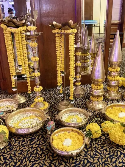 A collection of traditional brass artifacts, including diyas and urlis, decorated with marigold flowers to enhance the ethnic elegance of a ceremony.