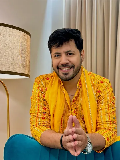 A seated pose in the yellow kurta, hands clasped. This conveys a sense of readiness and calm confidence before the show begins.