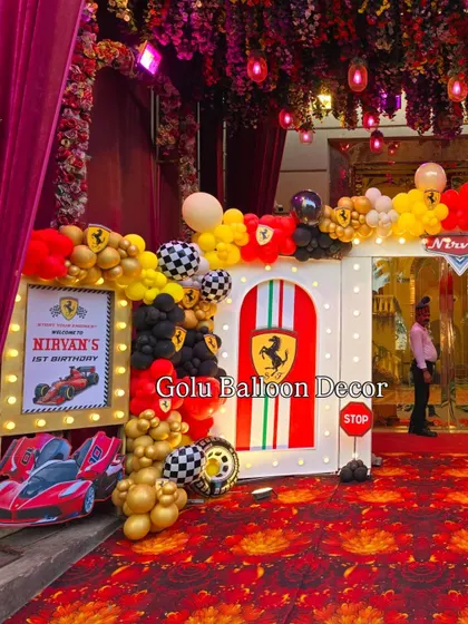 The entrance to Nirvan's first birthday, featuring a Ferrari-themed arch with red, yellow, and black balloons and a light-up welcome sign.