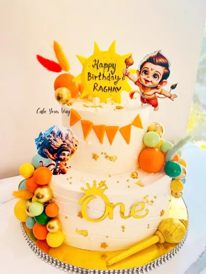 Celebrating the spirit of Bal Hanuman with this vibrant two-tier cake, complete with his Gada and other divine elements.