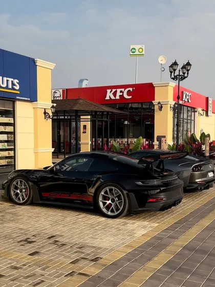 We are a popular meet-up spot for car enthusiasts. Here, a sleek Porsche GT3 and a Toyota Supra are seen parked outside our KFC outlet, showcasing the high-energy vibe you can expect.