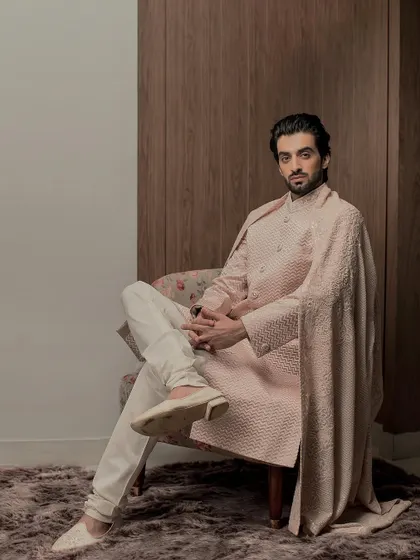 A seated portrait showcasing the comfortable yet structured fit of our rose gold sherwani. The tonal embroidery and matching stole create a cohesive and effortlessly elegant look for any formal occasion.