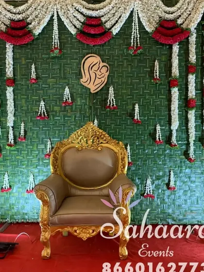 A close-up of our traditional baby shower backdrop. The design features a woven green mat, garlands of jasmine and roses, and a wooden cutout symbolizing motherhood.
