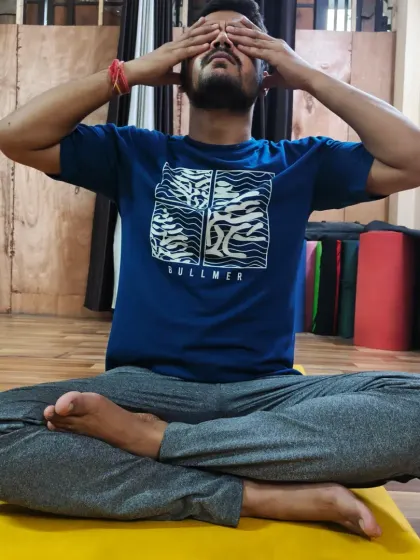 A male student practices Bhramari Pranayama, demonstrating the Shanmukhi Mudra to close off the senses. This helps to turn the awareness inward, deepening the meditative experience.