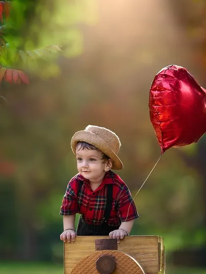All aboard for a happy birthday ride. This toddler portrait uses a toy train prop and a heart-shaped balloon to create a sweet and celebratory scene in a beautiful, naturally lit park.