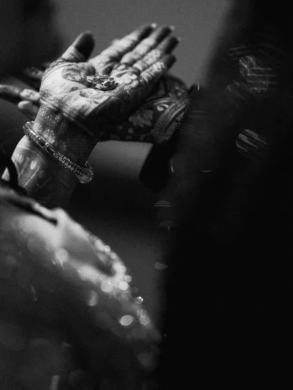 A close-up, black and white shot of hands during a ritual. The focus on this small, significant detail, with the sparkling water, creates a powerful and symbolic image.