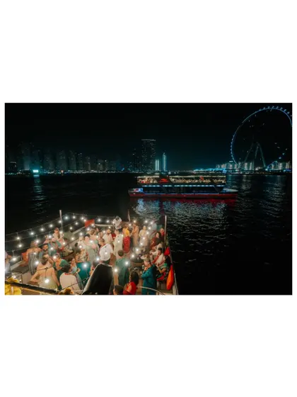 The entire wedding party dancing the night away on a yacht, with the glittering lights of Dubai in the background.