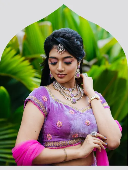 The model adjusts her jewelry, giving a better view of the neckline and embroidery on the velvet blouse. The ensemble is designed for elegance and poise.