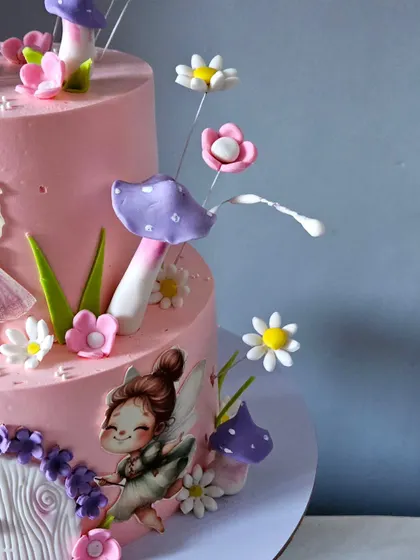 A detail shot of the side of the fairy cake, highlighting the edible mushrooms and printed fairy illustrations that add depth and storytelling to the design.