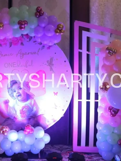 A circular, backlit photo backdrop featuring the birthday girl with fairy wings, framed by a pastel balloon garland. This creates a perfect spot for memorable photos.