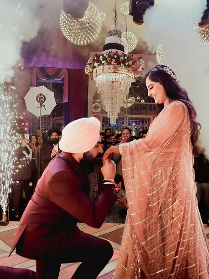 A romantic gesture as the groom kisses the bride's hand after the proposal. The smoke and lights create a dreamy atmosphere.