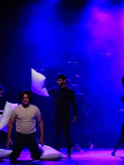 Dancers interact with pillows on a stage filled with purple and blue light during "ME & MY PILLOW." This scene captures the chaotic and dreamlike quality of the contemporary piece.