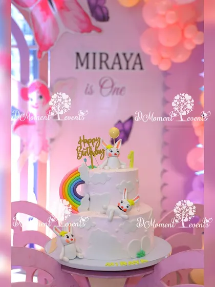 A whimsical two-tiered birthday cake for a bunny-themed party, decorated with cute fondant bunnies and a rainbow.