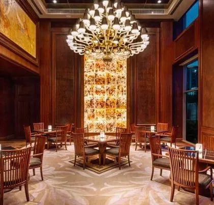 A dining area within the Sheraton Hotel, where a dramatic chandelier hangs above a backlit onyx wall feature. The combination of dark wood and warm light creates an elegant and intimate dining experience.
