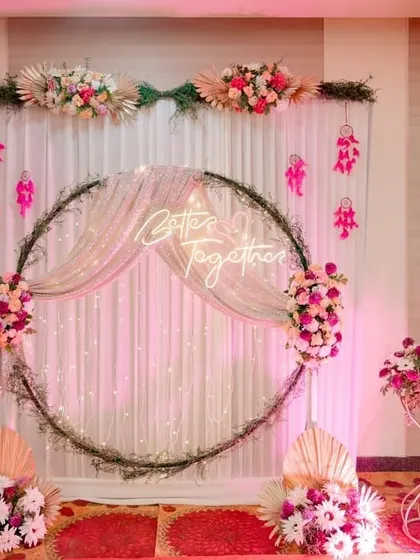 A beautiful photo booth with a "Better Together" neon sign. The circular frame is set against a backdrop of white drapes and fairy lights, and adorned with pastel floral arrangements.
