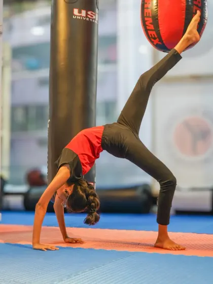 A young gymnast performs a graceful backbend, showcasing her flexibility while incorporating a medicine ball for an added challenge. We use various tools to enhance our students' training.