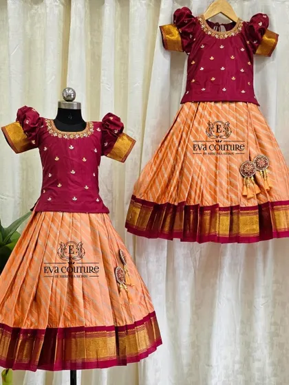 This is a beautiful sister-sister twinning set in a peach and maroon combination. Both pattu pavadai outfits feature a maroon blouse with gold butti work and a peach skirt with a traditional zari border.