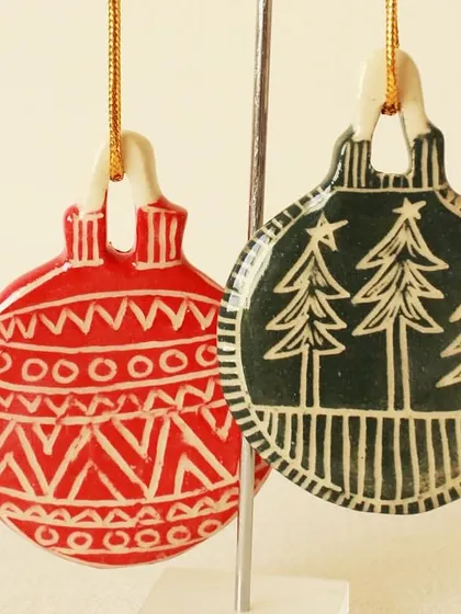 A pair of red and green ornaments with carved tribal and forest patterns. The contrast between the color and the revealed white clay makes the designs pop.