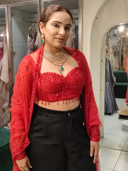 A client trying on a layered Polki necklace with an emerald drop. While it has traditional elements, its styling with a modern red bustier shows its versatility for fusion looks.