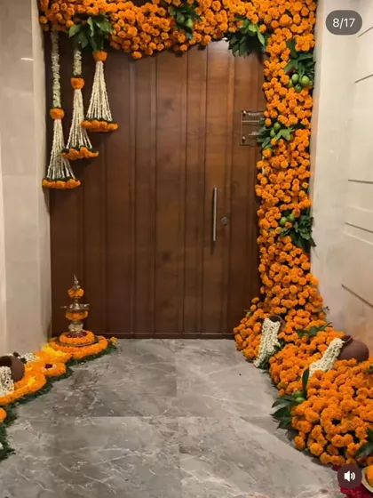 I make your home's entrance feel truly festive and welcoming. This traditional doorway decoration features dense garlands of fresh orange marigolds, accented with hanging jasmine tassels and a floral rangoli, setting a perfect tone for any celebration like Diwali or a housewarming pooja.