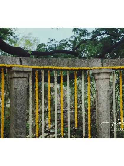 A stone pillar arch is decorated with hanging garlands of marigolds and chrysanthemums, creating a beautiful and traditional backdrop.