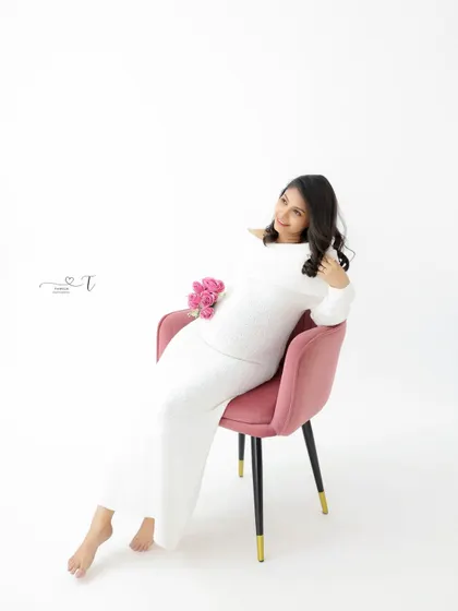 A chic and modern portrait. The mom-to-be relaxes in a stylish pink chair, her all-white outfit creating a clean and minimalist aesthetic.